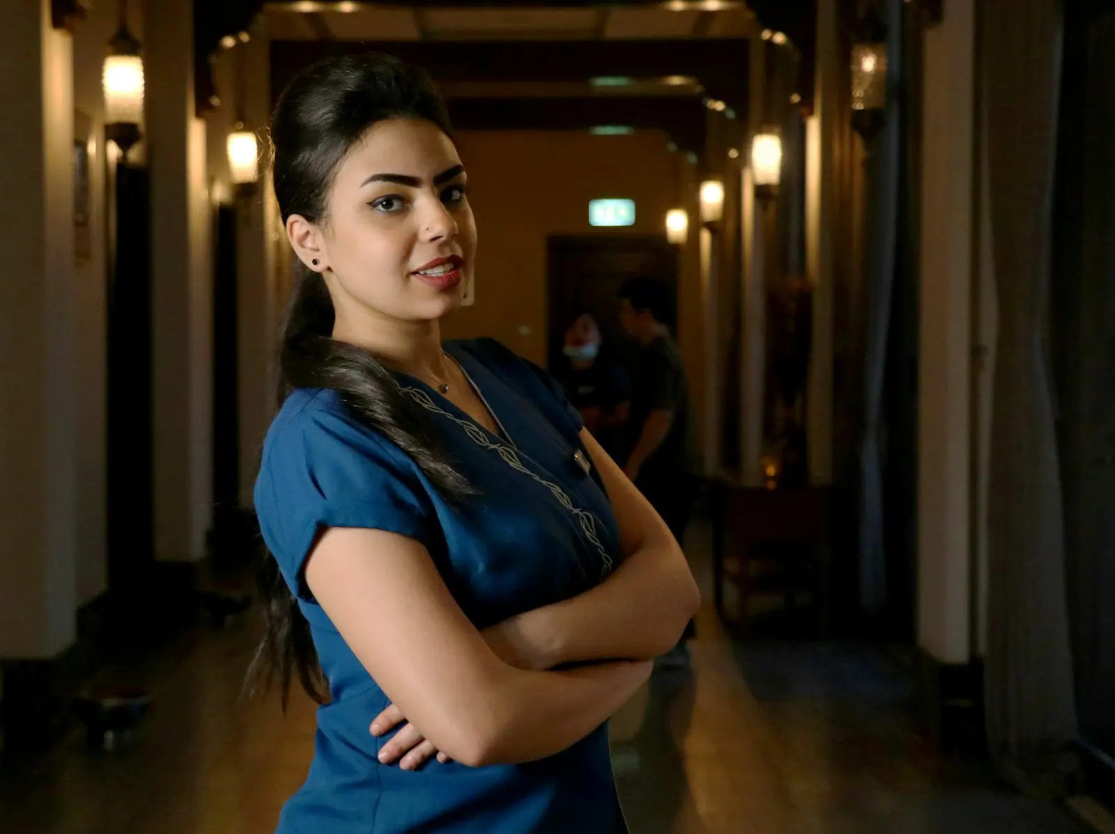 A nurse standing in a dim hospital corridor with folded arms